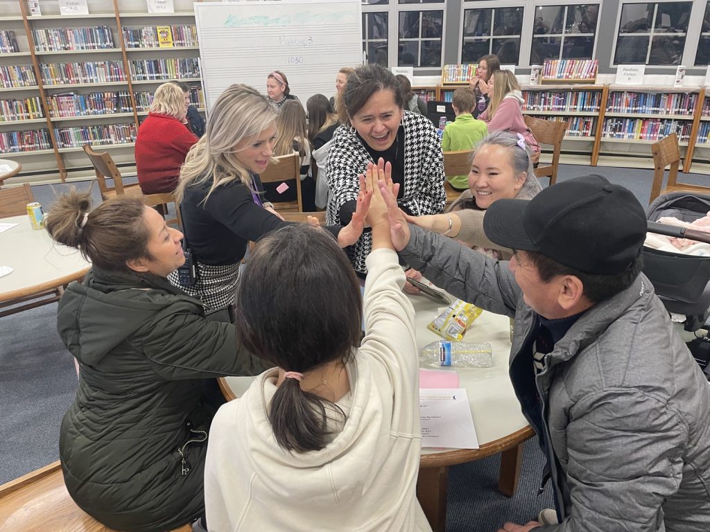 Adults and students high five over a circular table in a library.